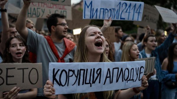 A woman chants while holding a banner that reads, “Corruption Applauds,” during a protest against a law targeting anti-corruption institutions in central Kiev, Ukraine, Tuesday, July 22, 2025 - Sputnik International