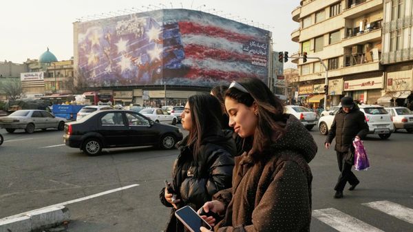 People walk past a billboard depicting a damaged U.S. aircraft carrier with disabled fighter jets on its deck and a sign reading in Farsi and English, If you sow the wind, you'll reap the whirlwind, at Enqelab-e-Eslami (Islamic Revolution) Square in Tehran, Iran, Sunday, Jan. 25, 2026. - Sputnik International