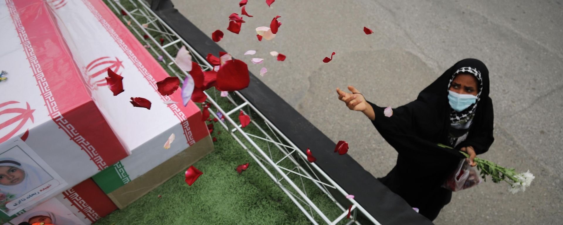 A woman throws rose petals on the coffins during funeral of mostly children killed in what Iranian officials said was an Israeli-U.S. strike Feb. 28 on a girls' elementary school in Minab, Iran, Tuesday, March 3, 2026. (Amirhossein Khorgooei/ISNA via AP) - Sputnik International, 1920, 04.03.2026