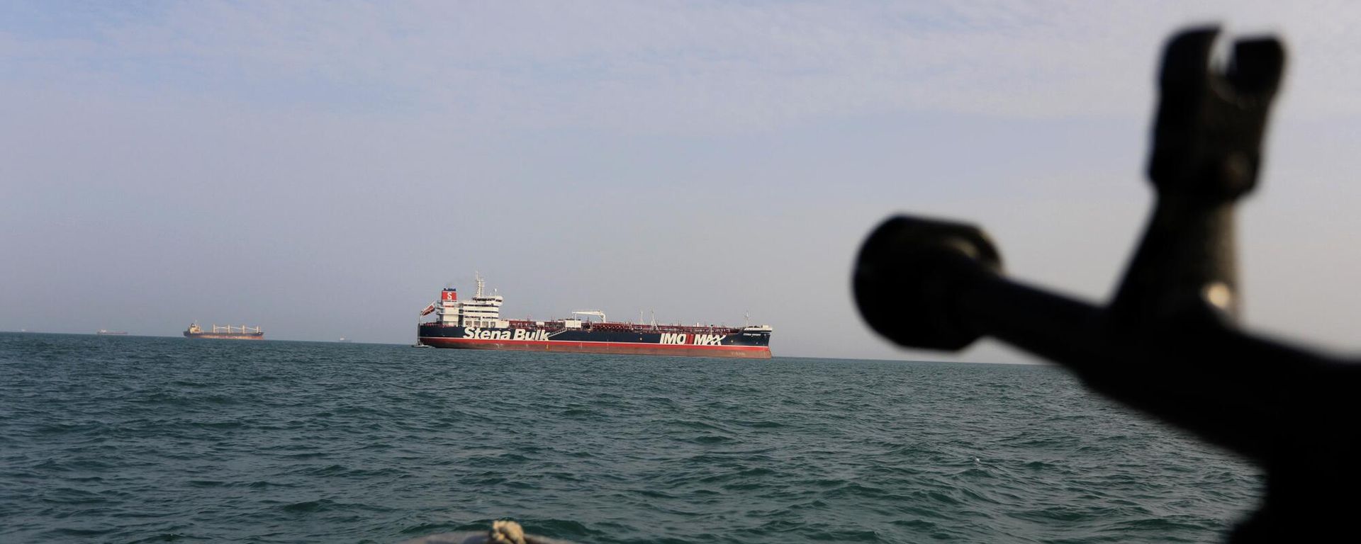 In this Sunday, July 21, 2019 photo, a speedboat of Iran's Revolutionary Guard trains a weapon toward the British-flagged oil tanker Stena Impero, which was seized in the Strait of Hormuz on Friday by the Guard, in the Iranian port of Bandar Abbas. Global stock markets were subdued Monday while the price of oil climbed as tensions in the Persian Gulf escalated after Iran's seizure of a British oil tanker on Friday. In this Sunday, July 21, 2019 photo, a speedboat of Iran's Revolutionary Guard trains a weapon toward the British-flagged oil tanker Stena Impero, which was seized in the Strait of Hormuz on Friday by the Guard, in the Iranian port of Bandar Abbas. Global stock markets were subdued Monday while the price of oil climbed as tensions in the Persian Gulf escalated after Iran's seizure of a British oil tanker on Friday. - Sputnik International, 1920, 06.04.2026