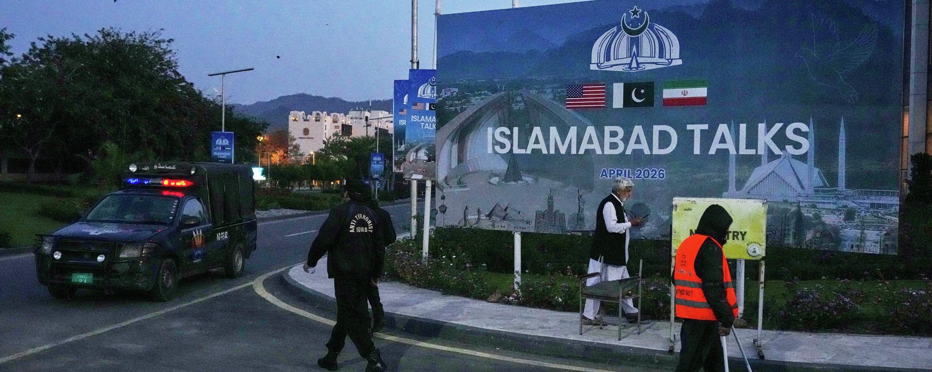 A worker cleans the street as police officers walks towards their vehicle outside a media center close to Serena Hotel, the venue for the U.S. Iran officials meeting, in Islamabad, Pakistan, Sunday, April 12, 2026. - Sputnik International, 1920, 17.04.2026
