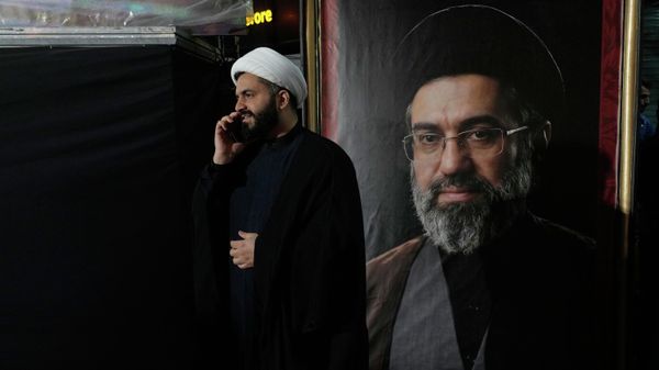 A cleric speaks on his cellphone next to a portrait of Iran's Supreme Leader Ayatollah Mojtaba Khamenei during a pro-government gathering near the residence where his father, former Supreme Leader Ayatollah Ali Khamenei, was killed during US and Israeli strikes on Feb. 28, in Tehran, Iran, Monday, May 18, 2026. - Sputnik International