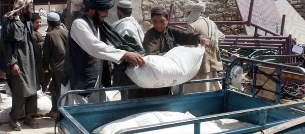 Afghans put a sack of wheat on the carrier back of a motor bike during a food distribution to displaced families from Helmand province. - Sputnik International