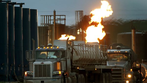 Drivers and their tanker trucks, capable of hauling water and fracking liquid line up near a natural gas burn off flame and storage tanks in Williston, N.D. - Sputnik International