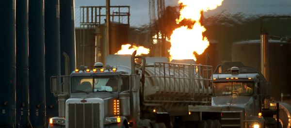 Drivers and their tanker trucks, capable of hauling water and fracking liquid line up near a natural gas burn off flame and storage tanks in Williston, N.D. - Sputnik International