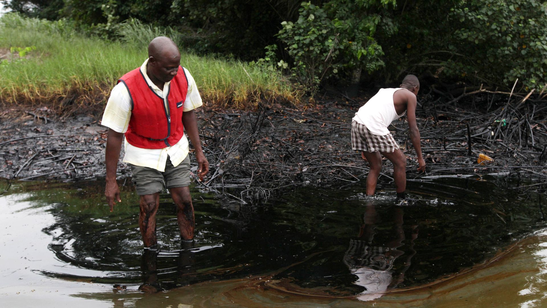In this June 20, 2010 file photo, men walk in an oil slick covering a creek near Bodo City in the oil-rich Niger Delta region of Nigeria In this June 20, 2010 file photo, men walk in an oil slick covering a creek near Bodo City in the oil-rich Niger Delta region of Nigeria - Sputnik International, 1920, 05.10.2022