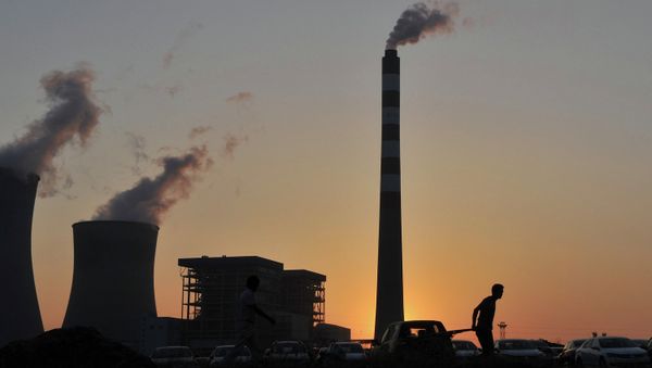 A worker pulls a cart in front of the smoking chimneys of a power plant - Sputnik International