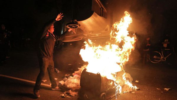 A protester throws a trash can on a fire during a demonstration in Oakland, California following the grand jury decision in the shooting of Michael Brown in Ferguson, Missouri A protester throws a trash can on a fire during a demonstration in Oakland, California following the grand jury decision in the shooting of Michael Brown in Ferguson, Missouri - Sputnik International