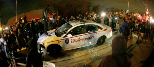 A protester squirts lighter fluid on a police car as the car windows are shuttered near the Ferguson Police Department after the announcement of the grand jury decision not to indict police officer Darren Wilson in the fatal shooting of Michael Brown, an unarmed black 18-year-old in Ferguson - Sputnik International