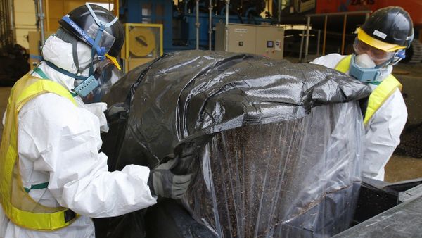 Workers wearing protective gear wrap a compressed radioactive waste in a protective storage bag at a temporary waste storage site - Sputnik International