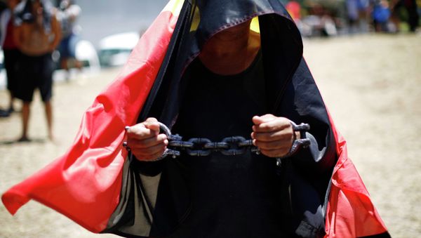A protester demanding human rights for Australia's Aboriginal community wears symbolic shackles as he is draped in the Aboriginal flag. - Sputnik International