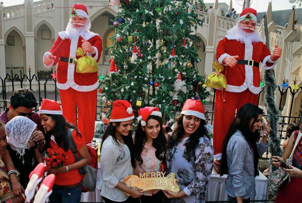 Indian girls pose for photos near statues of decorative Santa Claus outside a church on Christmas in Mumbai, India - Sputnik International