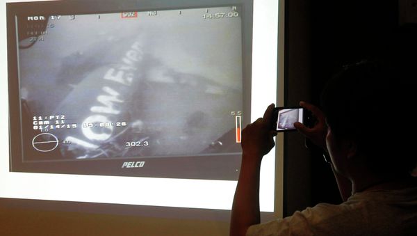 A journalist takes a photograph of an image believed to be of the fuselage of AirAsia Flight QZ8501 - Sputnik International