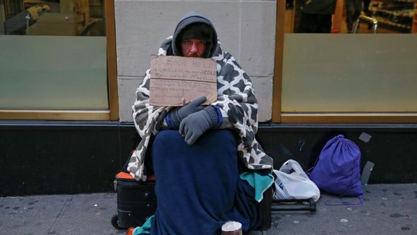 A man holding up a sign stating he is 'homeless, hungry and cold' sits along 7th avenue in New York - Sputnik International