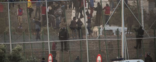 Sub-Saharan migrants sit on a metal fence that divides Morocco and the Spanish enclave of Melilla Sub-Saharan migrants sit on a metal fence that divides Morocco and the Spanish enclave of Melilla - Sputnik International