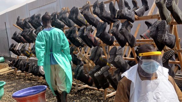 Health care workers walk past boots that were washed to prevent the spread of the Ebola virus inside a USAID, funded Ebola clinic in Monrovia, Liberia, Friday, Jan. 30, 2015. The World Health Organization says officials are now focused on ending the biggest-ever Ebola outbreak rather than just slowing the virus’ spread. - Sputnik International