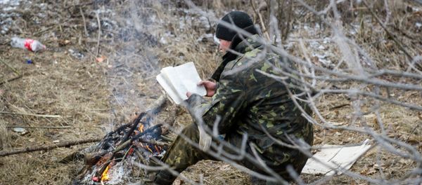 A Ukrainian serviceman reads a book as he warms himself by a camp fire in Svitlodarsk, approaching Debaltseve on February 15, 2015 - Sputnik International