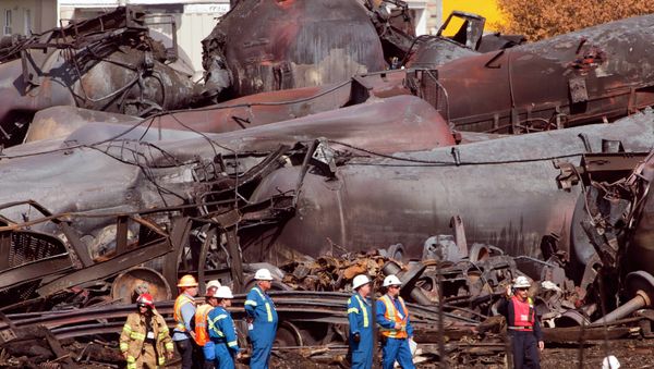 In this July 6, 2013, file photo, workers stand before mangled tanker cars at the crash site of the train derailment and fire in Lac-Megantic, Quebec, Canada. - Sputnik International