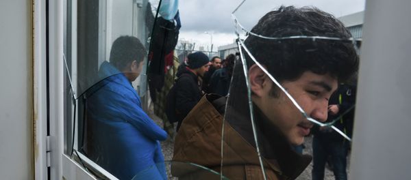 Migrants stand behind a broken window at the Foreigners Detention Center in Amygdaleza, Greece, north of the capital Athens, following the apparent suicide of a Pakistani detainee on Saturday, Feb. 14, 2015 - Sputnik International