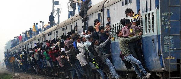 Indian passengers stand and hang onto a train as it departs from a station on the outskirts of New Delhi on February 25, 2015 - Sputnik International