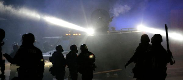 Police in riot gear stand around an armored vehicle as smoke fills the streets Tuesday, Nov. 25, 2014, in Ferguson, Mo. - Sputnik International