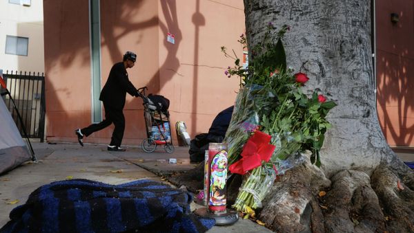 A pedestrian walks past flowers and candles placed on a sidewalk near where a man was shot and killed by police in the Skid Row section of downtown Los Angeles A pedestrian walks past flowers and candles placed on a sidewalk near where a man was shot and killed by police in the Skid Row section of downtown Los Angeles - Sputnik International