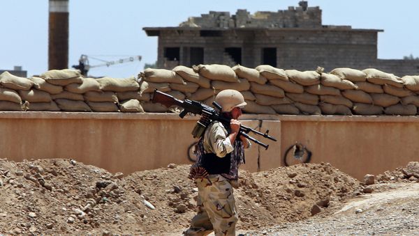 A Kurdish Peshmerga fighter carries his weapon walks onto his base, where two flags of the Islamic State in Iraq and the Levant (ISIL) are seen on a building, right, and water tower, left, at the front line with the al-Qaida-inspired militants in Tuz Khormato, 100 kilometers (62 miles) south of the oil rich province of Kirkuk, northern Iraq. - Sputnik International