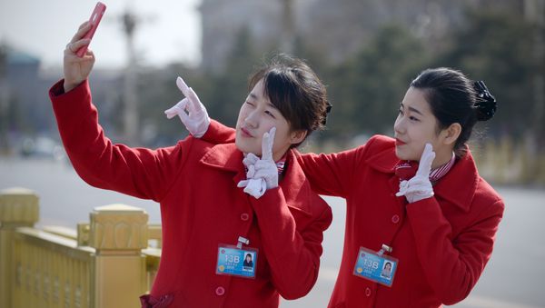 Chinese hostesses use a mobile phone to take a photo during the third session of the 12th National People's Congress outside the Great Hall of the People in Beijing - Sputnik International