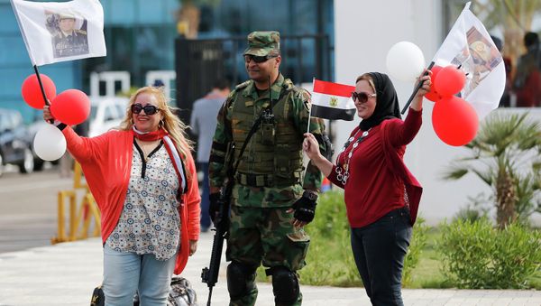 Egyptian women wave flags with pictures of Egyptian President Abdel Fattah al-Sisi, next to a soldier outside a conference centre hosting the Egypt Economic Development Conference (EEDC) in Sharm el-Sheikh, in the South Sinai governorate, south of Cairo, March 14, 2015 - Sputnik International