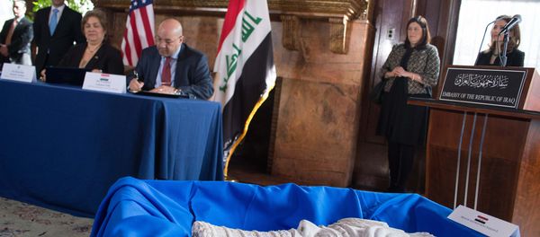 Assistant Secretary of Homeland Security for Immigration and Customs Enforcement Sarah Saldaña (seated, L) and Iraqi Ambassador to the US Lukman Faily sign documents behind a sculpture of the head of Assyrian King Sargon II during a ceremony to repatriate more than 60 Iraqi artifacts which had been smuggled into the US at the Iraqi consulate in Washington, DC, on March 16, 2015. - Sputnik International