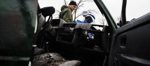 An armed man and an international observer of the Organization for Security and Co-operation in Europe (OSCE) stand next a destroyed car after shelling during an OSCE inspection tour near the village of Shirokino. - Sputnik International