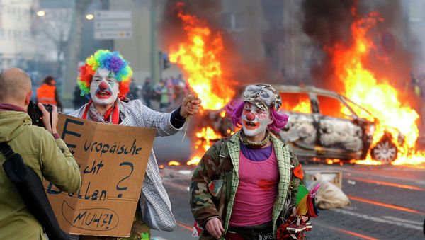 Demonstrators dressed as clowns pass by a burning police car Wednesday, March 18, 2015 in Frankfurt, Germany. - Sputnik International