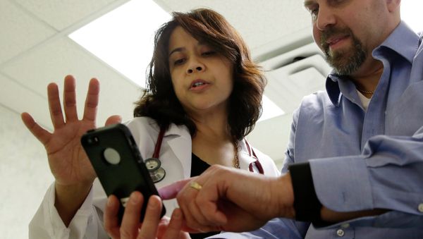 A doctor looks at data on a smart phone synchronized to a new Fitbit Surge worn by a patient. - Sputnik International