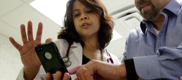 A doctor looks at data on a smart phone synchronized to a new Fitbit Surge worn by a patient. - Sputnik International