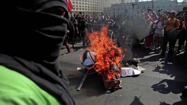 A masked demonstrator stands next to a pile of debris set on fire during a protest near La Moneda Palace in Santiago, Chile, Thursday, April 16, 2015. Thousands of students marched through the streets of Chile’s capital to protest recent corruption scandals and to complain about delays in a promised education overhaul. While it was largely peaceful, violence broke out at the end when hooded protesters threw rocks and gasoline bombs at police. At least one officer was injured. - Sputnik International