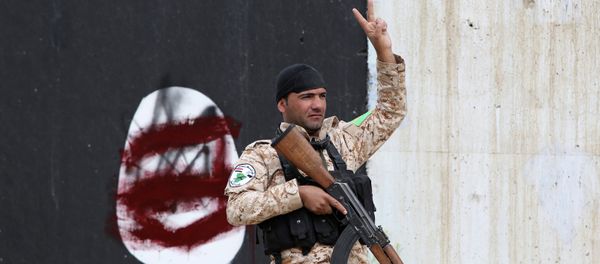 A member of the Iraqi security forces flashes the sign for victory in front of a defaced Islamist flag in Tikrit - Sputnik International