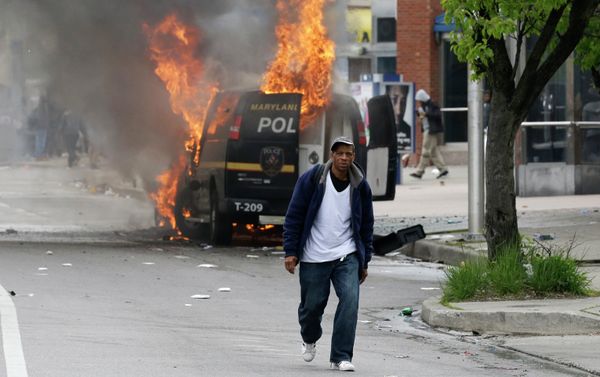 A man walks past a burning police vehicle, Monday, April 27, 2015, during unrest following the funeral of Freddie Gray in Baltimore. Gray died from spinal injuries about a week after he was arrested and transported in a Baltimore Police Department van. - Sputnik International