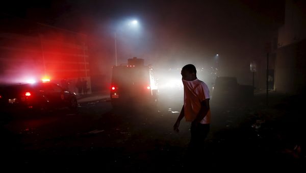 A protester walks through the smoke of burning Baltimore buildings set ablaze by rioters as a police armored car drives past during clashes in Baltimore, Maryland April 27, 2015. Maryland Governor Larry Hogan declared a state of emergency and activated the National Guard to address the violence in Baltimore, his office said on Monday. A protester walks through the smoke of burning Baltimore buildings set ablaze by rioters as a police armored car drives past during clashes in Baltimore, Maryland April 27, 2015. Maryland Governor Larry Hogan declared a state of emergency and activated the National Guard to address the violence in Baltimore, his office said on Monday. - Sputnik International