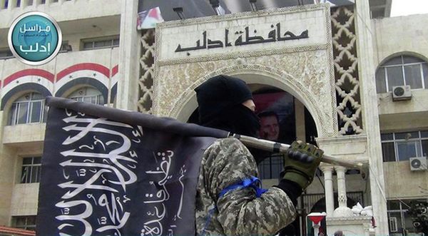 A fighter from Syria's al-Qaeda-linked Nusra Front holds his group flag as he stands in front of the governor building in Idlib province, north Syria. - Sputnik International