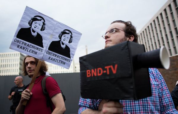 Demonstrators hold a poster showing a portrait of German Chancellor Angela Merkel reading surveillance Chancellor and a fake surveillance camera during a protest against the surveillance by the US National Security Agency, NSA. Demonstrators hold a poster showing a portrait of German Chancellor Angela Merkel reading surveillance Chancellor and a fake surveillance camera during a protest against the surveillance by the US National Security Agency, NSA. - Sputnik International