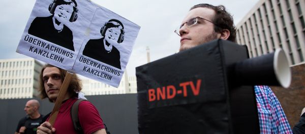 Demonstrators hold a poster showing a portrait of German Chancellor Angela Merkel reading surveillance Chancellor and a fake surveillance camera during a protest against the surveillance by the US National Security Agency, NSA. Demonstrators hold a poster showing a portrait of German Chancellor Angela Merkel reading surveillance Chancellor and a fake surveillance camera during a protest against the surveillance by the US National Security Agency, NSA. - Sputnik International