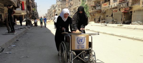 Residents of Syria's Yarmuk Palestinian refugee camp, south of Damascus, use a wheelchair to carry a box of goods distributed by the United Nations Relief and Works Agency (UNRWA) on July 17, 2014 - Sputnik International