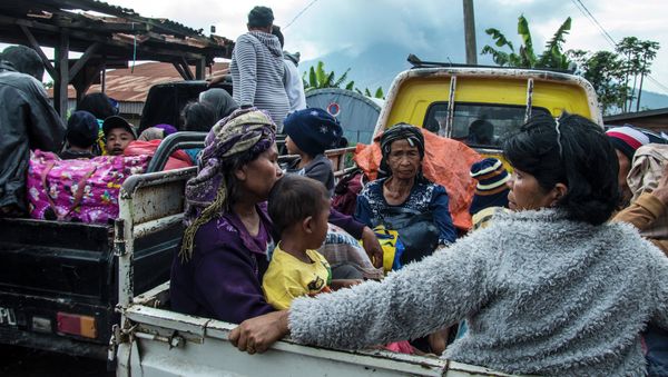 Residents are evacuated on farm vehicles at a village in the district of Karo near Mount Sinabung volcano, seen in the background, partly covered by clouds on June 3, 2015 - Sputnik International