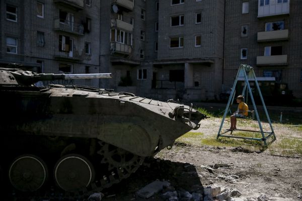 A boy sits on a swing near a building, which was damaged during fighting between Kiev and Donbass forces, as an armoured personnel carrier (APC) of the Ukrainian armed forces is seen nearby in Avdeyevka near Donetsk. June 7, 2015. - Sputnik International