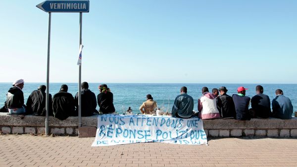 Migrants sit near a banner reading We are waiting fo a political response on the shores of the Mediterranean sea in the Italian Franco-Italian border city of Ventimiglia on June 15, 2015, as they wait to cross into France Migrants sit near a banner reading We are waiting fo a political response on the shores of the Mediterranean sea in the Italian Franco-Italian border city of Ventimiglia on June 15, 2015, as they wait to cross into France - Sputnik International
