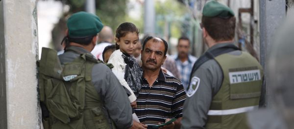 A Palestinian man carrying his daughter shows his identity card to Israeli border policemen at an Israeli checkpoint in the West bank city of Bethlehem June 26, 2015 - Sputnik International