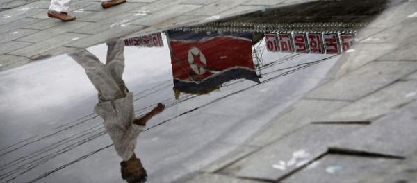A North Korean woman is reflected in a rain puddle as she walks past the country's national flag along the Kim Il Sung Square on Sunday, July 21, 2013, downtown Pyongyang, North Korea - Sputnik International
