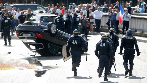 French riot police stand next to an overturned car as striking French taxi drivers demonstrate at the Porte Maillot to block the traffic on the Paris ring road during a national protest against car-sharing service Uber, in Paris, France, June 25, 2015 - Sputnik International