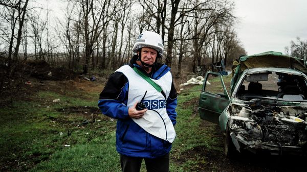 An International observer of the Organization for Security and Co-operation in Europe (OSCE) stands next to a destroyed car after shelling during an inspection tour near the village of Shirokino - Sputnik International