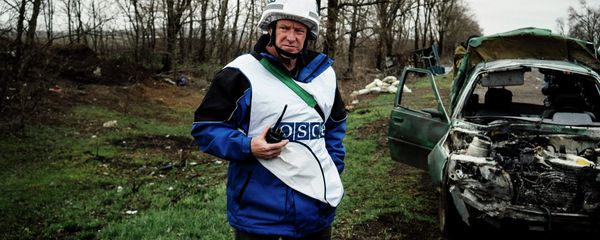 An International observer of the Organization for Security and Co-operation in Europe (OSCE) stands next to a destroyed car after shelling during an inspection tour near the village of Shirokino - Sputnik International